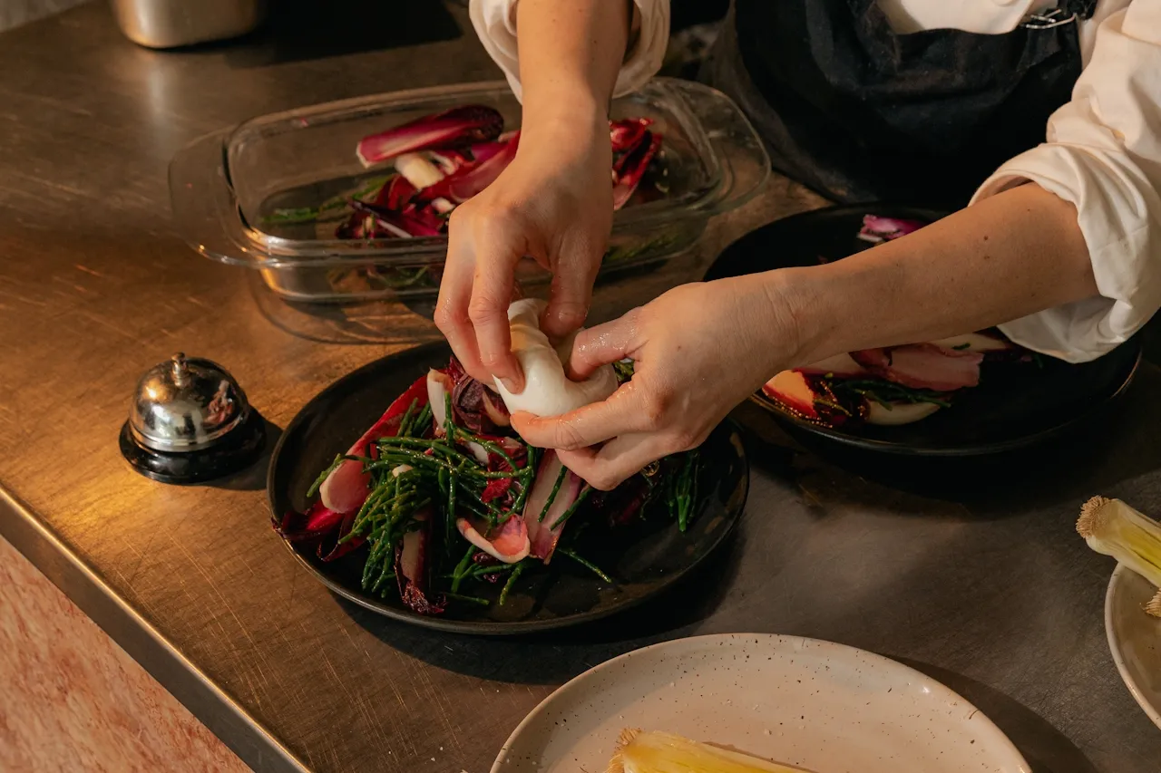 Chef's hands plating a dish in a restaurant kitchen