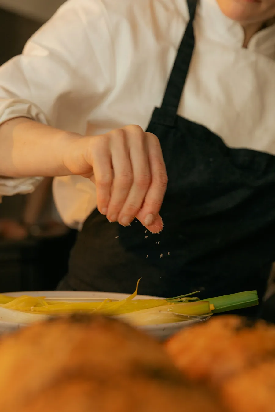 Chef seasoning over a plate in a kitchen